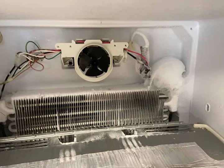Freezer compartment opened with frosted evaporator fins and fan motor